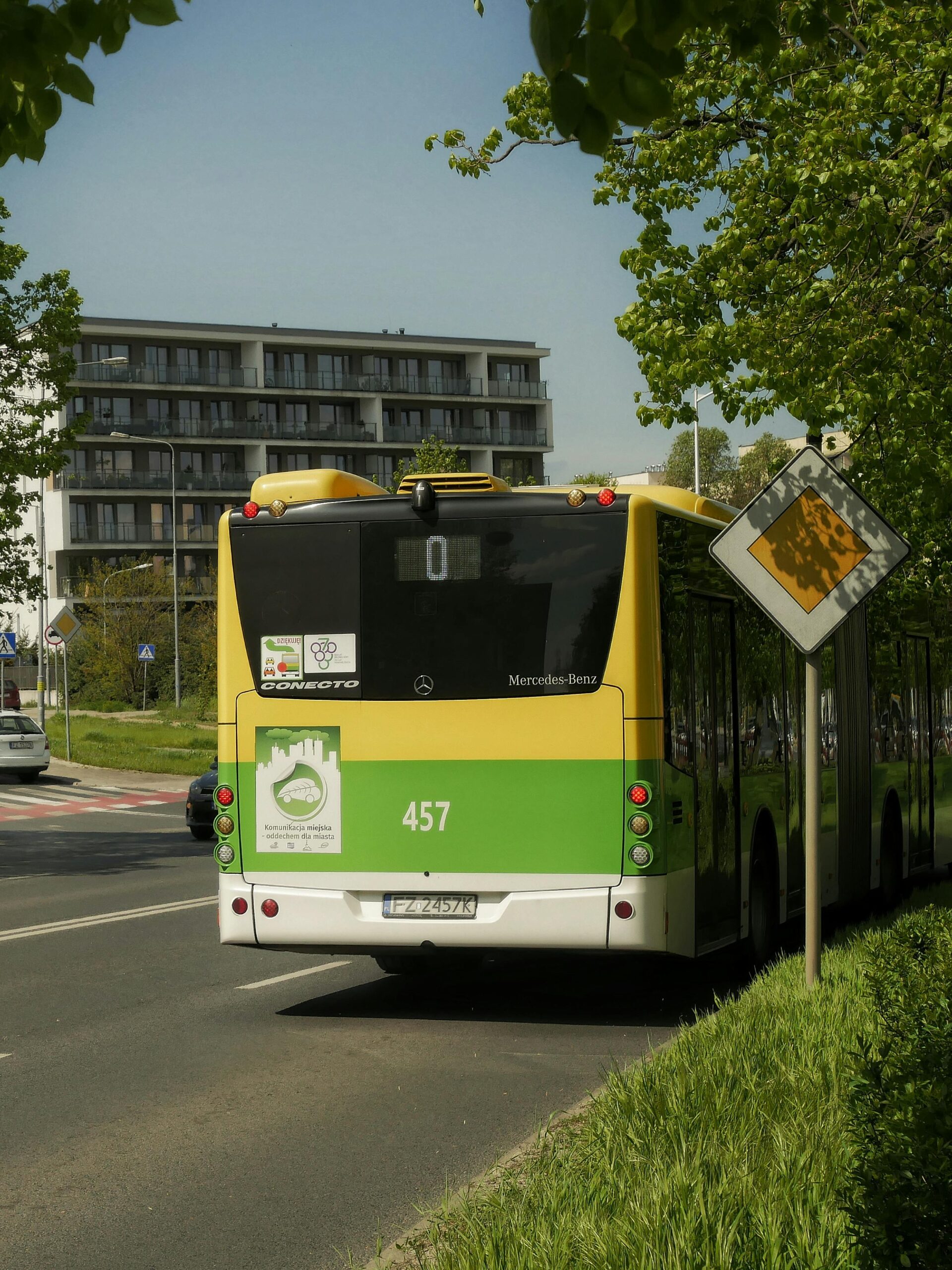 Zielono-żółty autobus miejski na ulicy wśród drzew