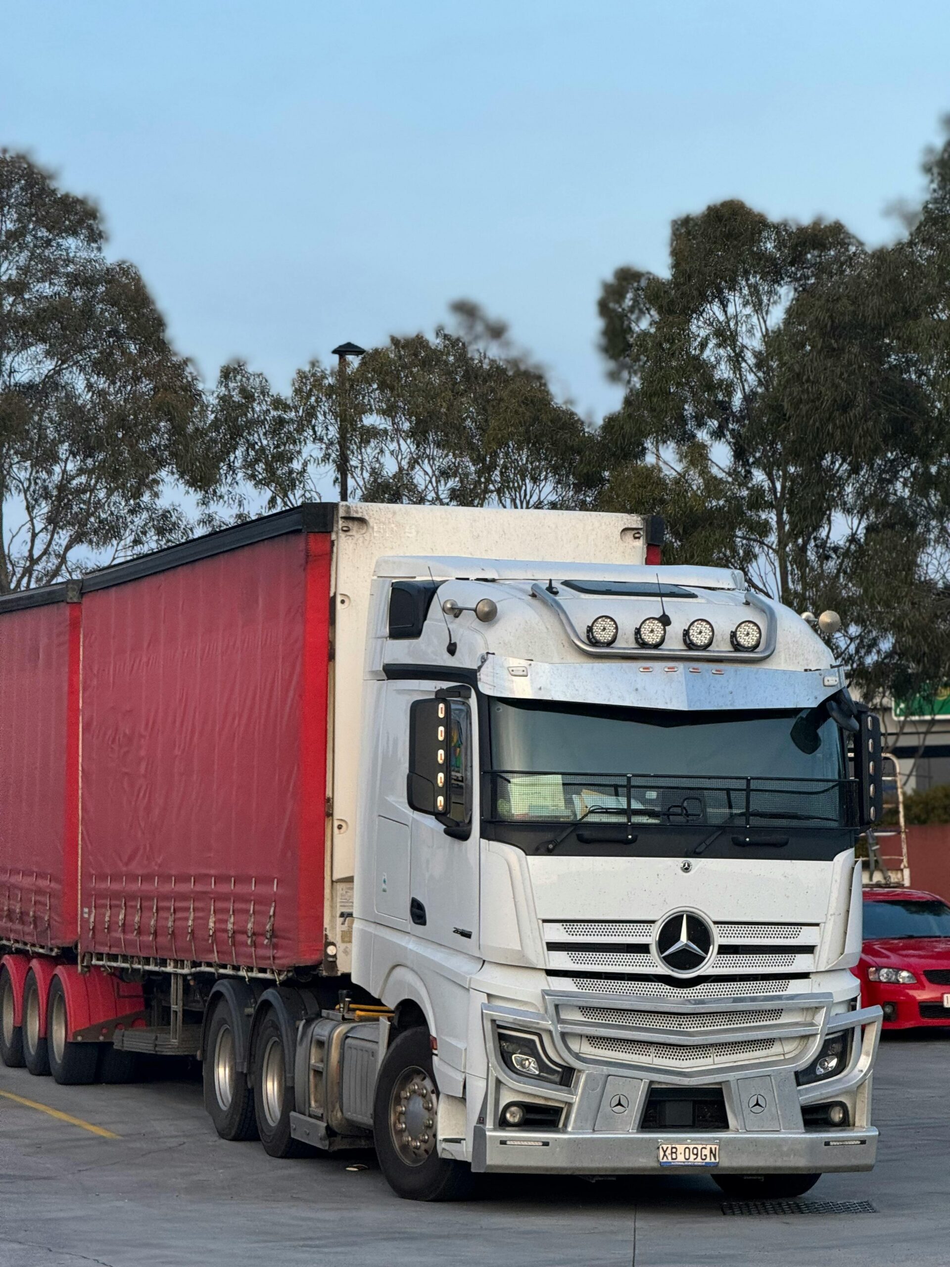 Biały Mercedes Actros z czerwoną naczepą na parkingu