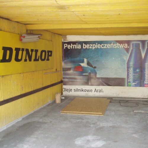 Wnętrze warsztatu samochodowego z logo Dunlop i reklamą olejów Aral